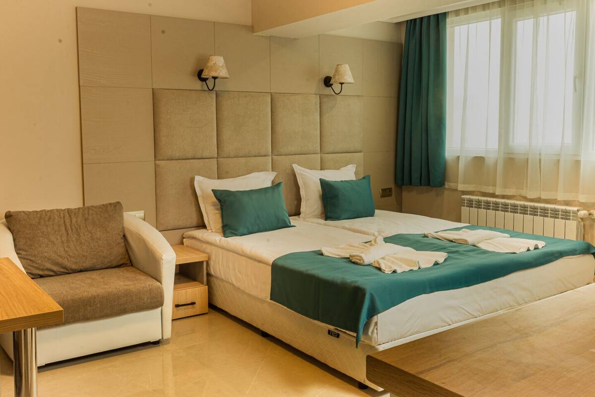 Una habitación de hotel con cama, una silla, una mesita de noche y una ventana con cortinas.