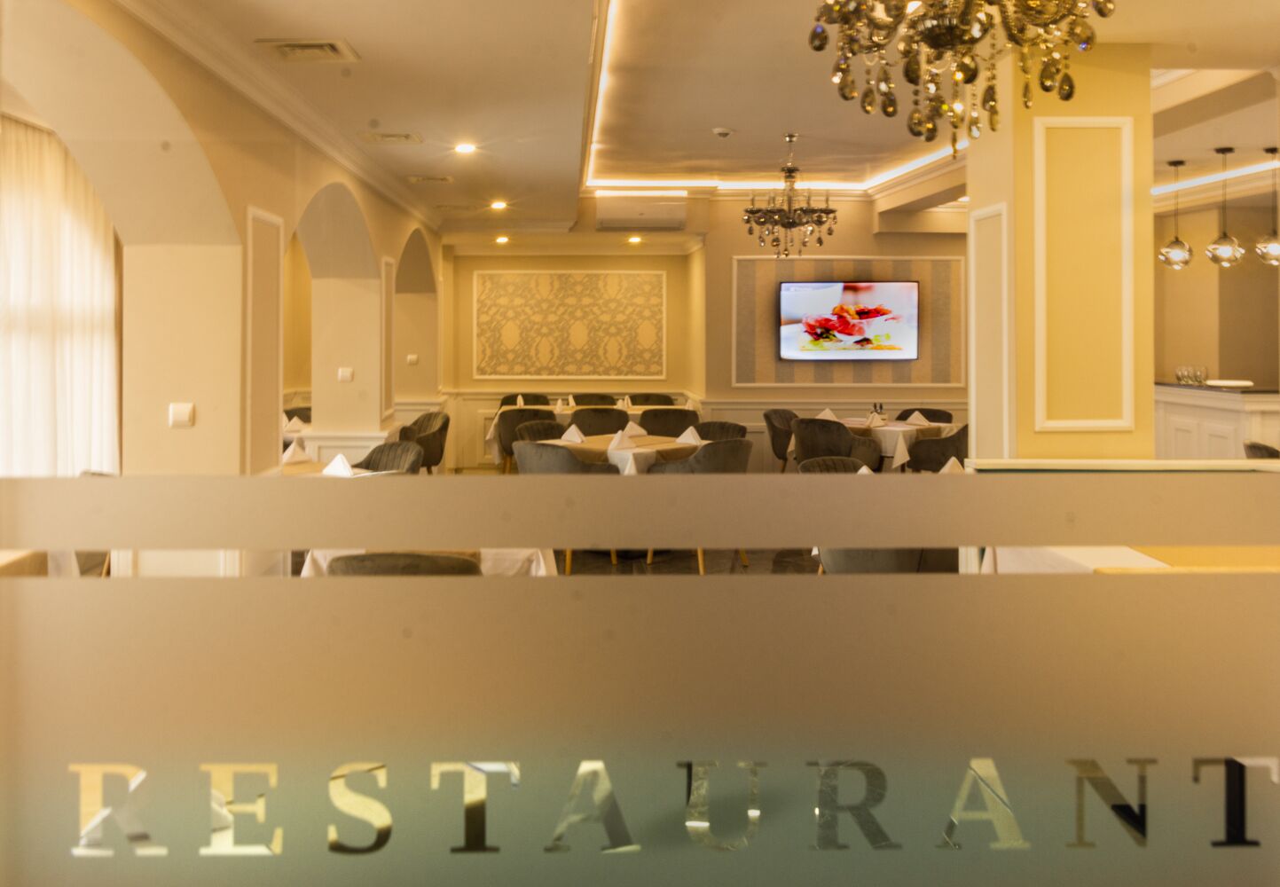 L’intérieur d’un restaurant, avec un lustre, un écran de télévision et une rangée de tables et de chaises.