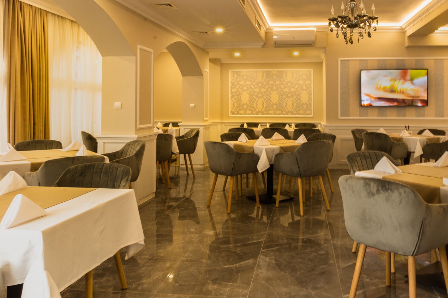 Un restaurant avec des tables et des chaises, un lustre et un téléviseur accroché au mur.