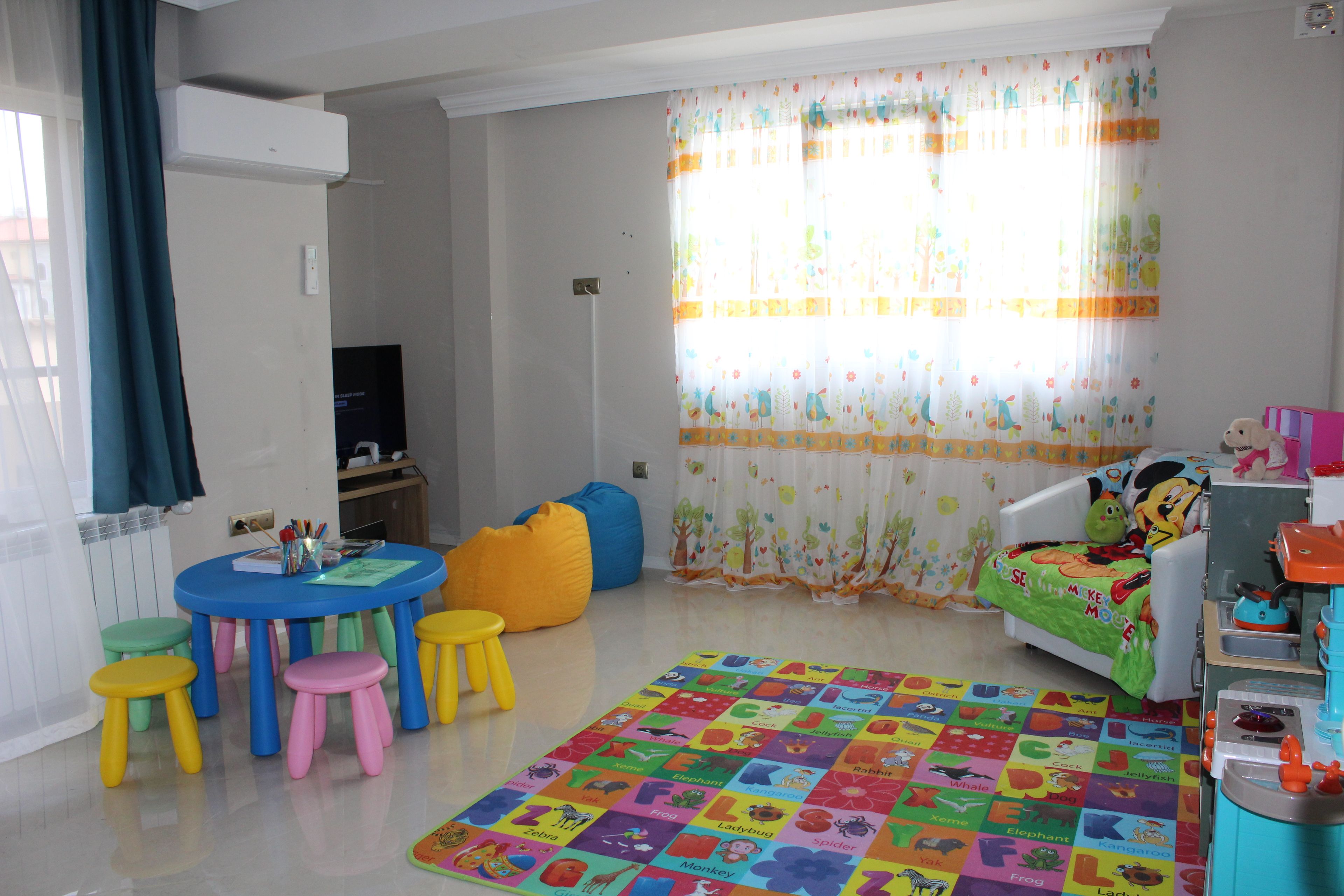 A child's playroom with a colorful alphabet rug, bean bags, and a small table with toys.