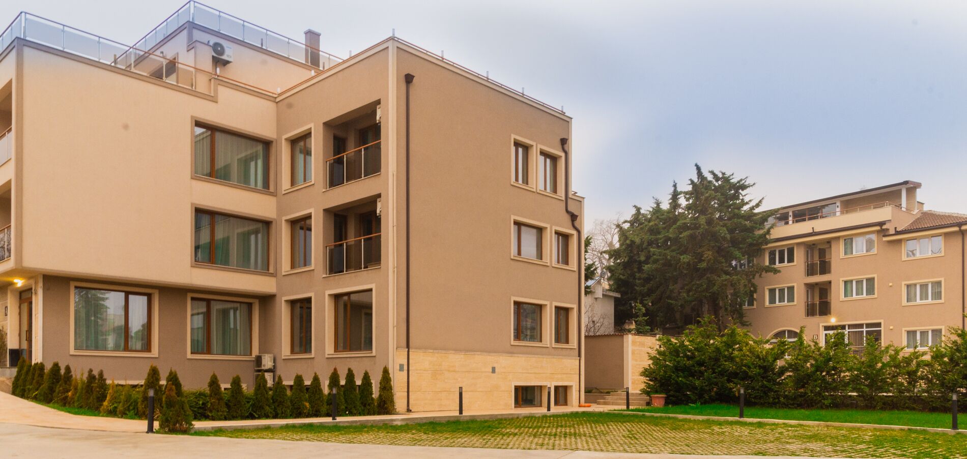 A multi-story residential building with a flat facade, large windows, and a small front garden.