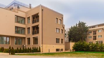 A multi-story residential building with a flat facade, large windows, and a small front garden.