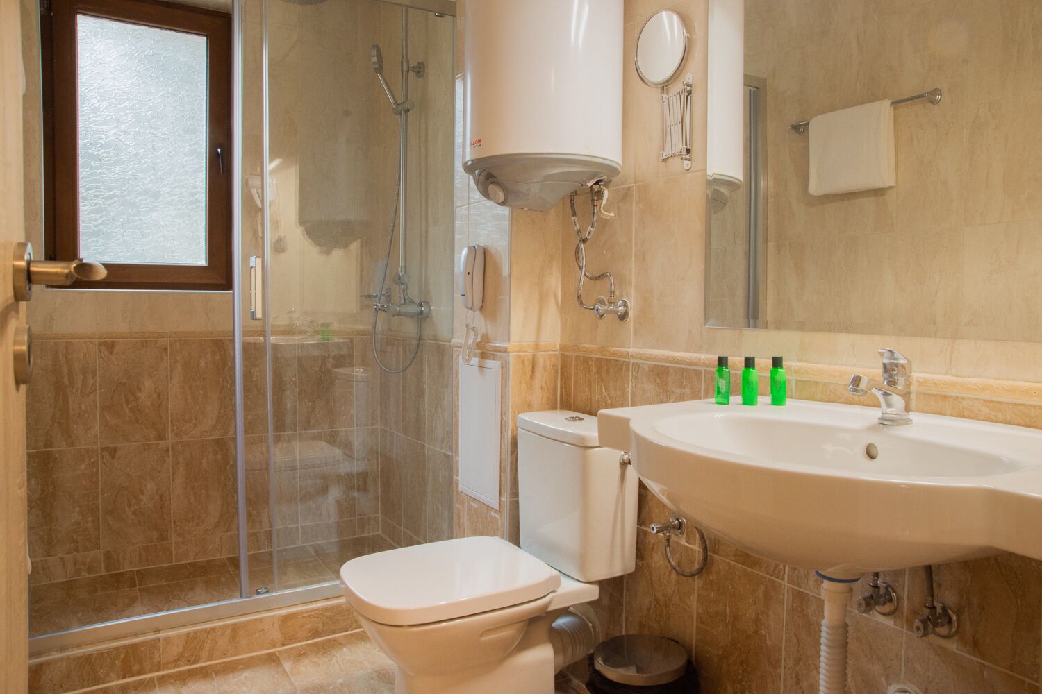 A bathroom with a glass-enclosed shower, a toilet, a sink with toiletries, and a mirror.