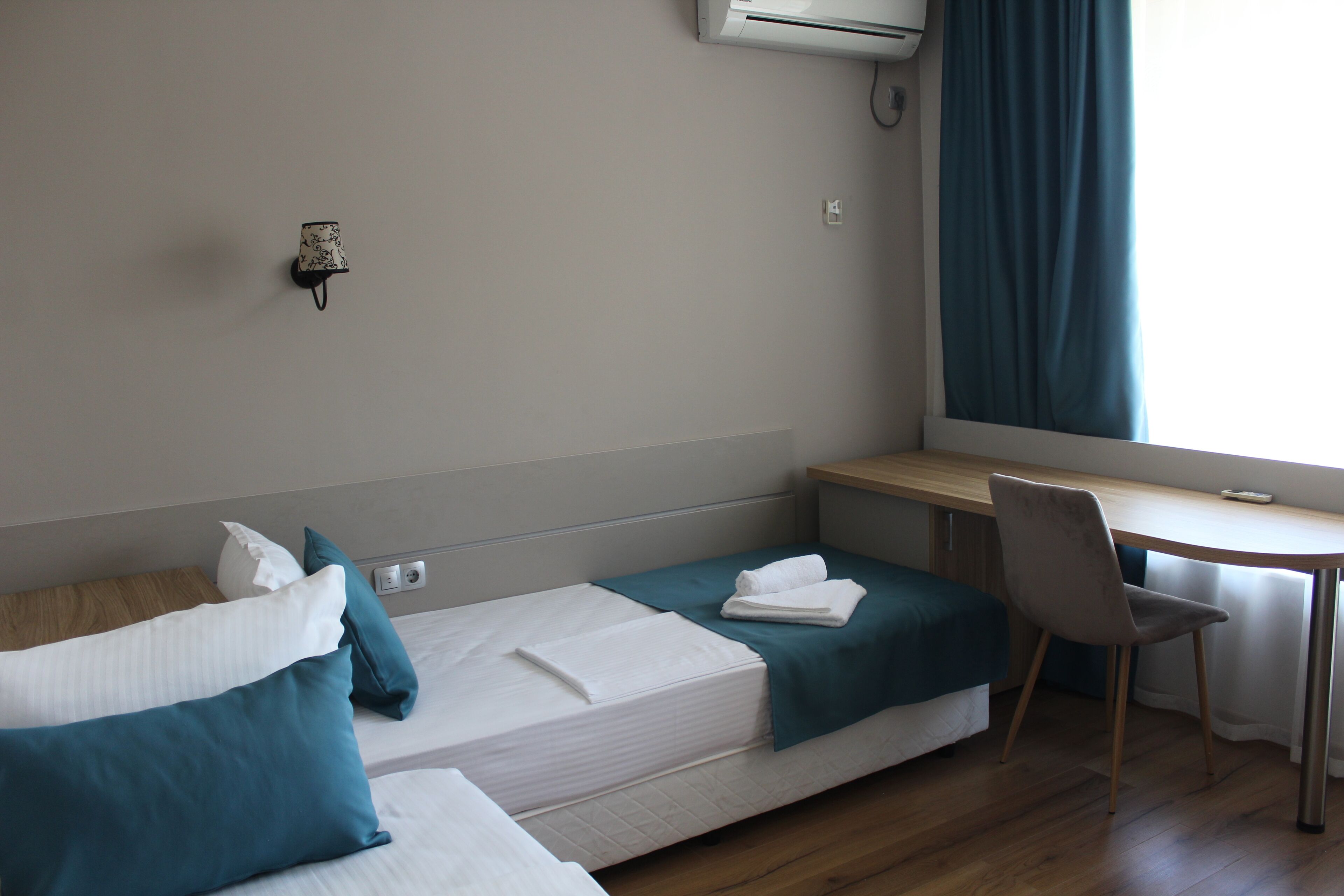 Een hotelkamer met twee enkele bedden, een bureau, een stoel en een airconditioning.