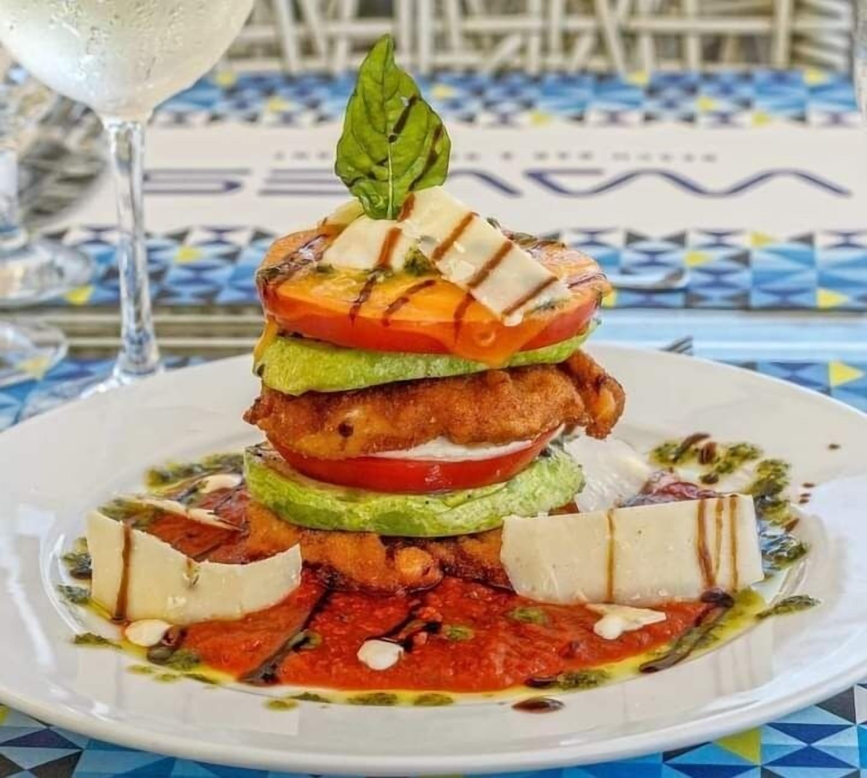 A plate of layered food with a glass of white beverage on a table with a blue and white patterned tablecloth.