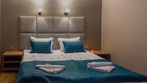 Een net opgemaakt bed met blauwgroene en witte beddengoed, twee bedlampen en een nachtkastje met een kaars.