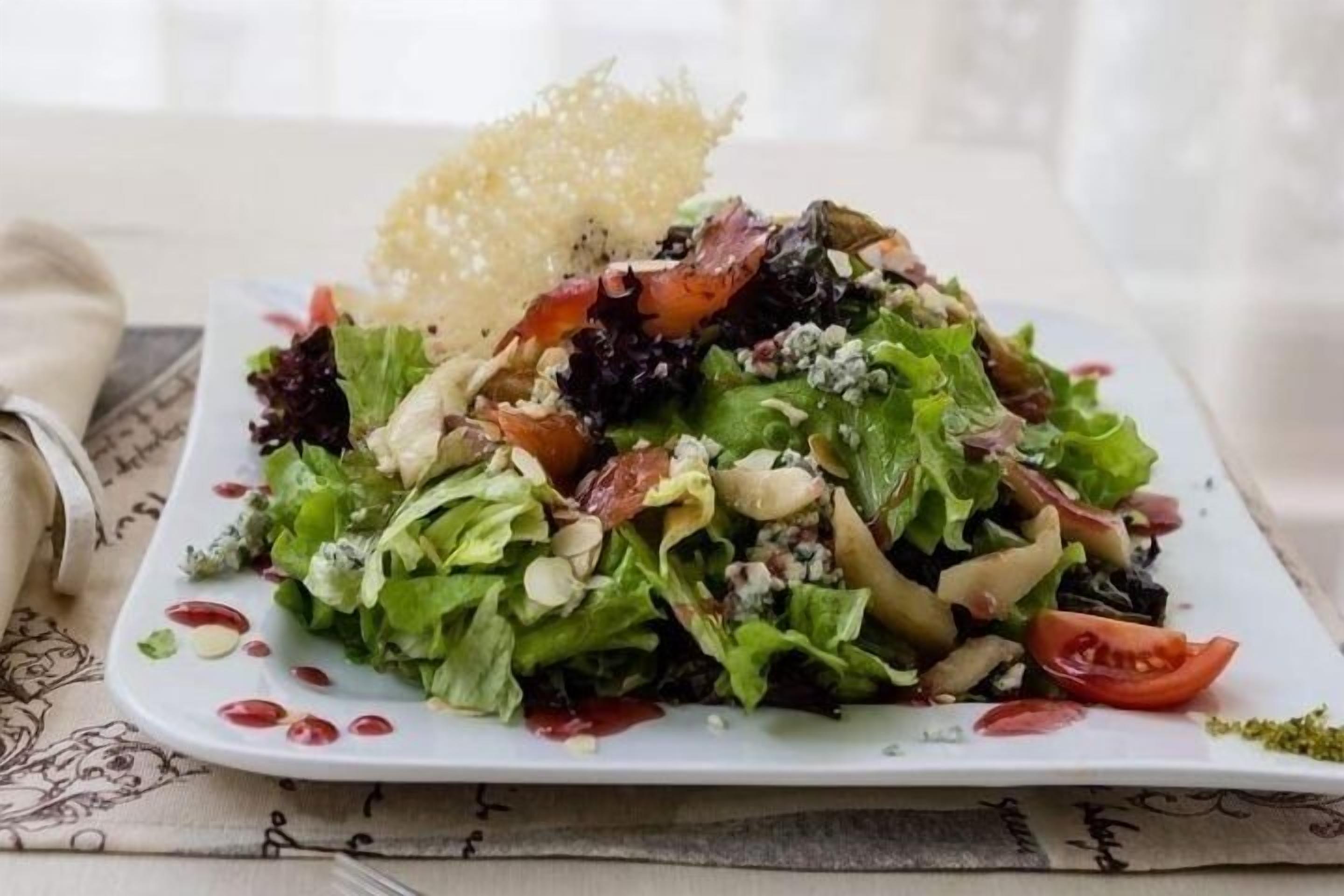 Ensalada de hojas verdes variadas con nueces, queso y un tomate cherry sobre un plato blanco.