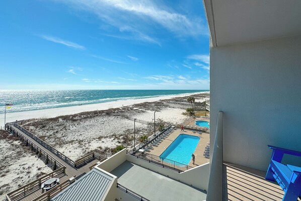 A beach view from a balcony with a pool and lounge chairs.