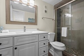A bathroom with a white vanity, a large mirror, a glass shower enclosure, and a white toilet.