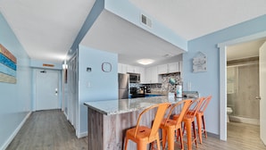 A modern kitchen with a central island, bar stools, and a clock on the wall. - HEART OF GULF SHORES, GULF-FRONT BALCONY, POOL! | BEACHBALL PROPERTIES (Gulf Shores)