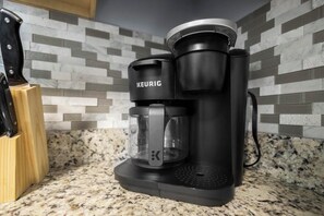 A Keurig coffee maker on a granite countertop with a knife block and a tiled backsplash.