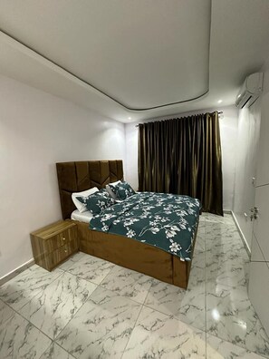 A modern bedroom with a wooden bed, a nightstand, and a marble floor. - Luxury 3bed Furnished Apartment at Ikate (Lekki)