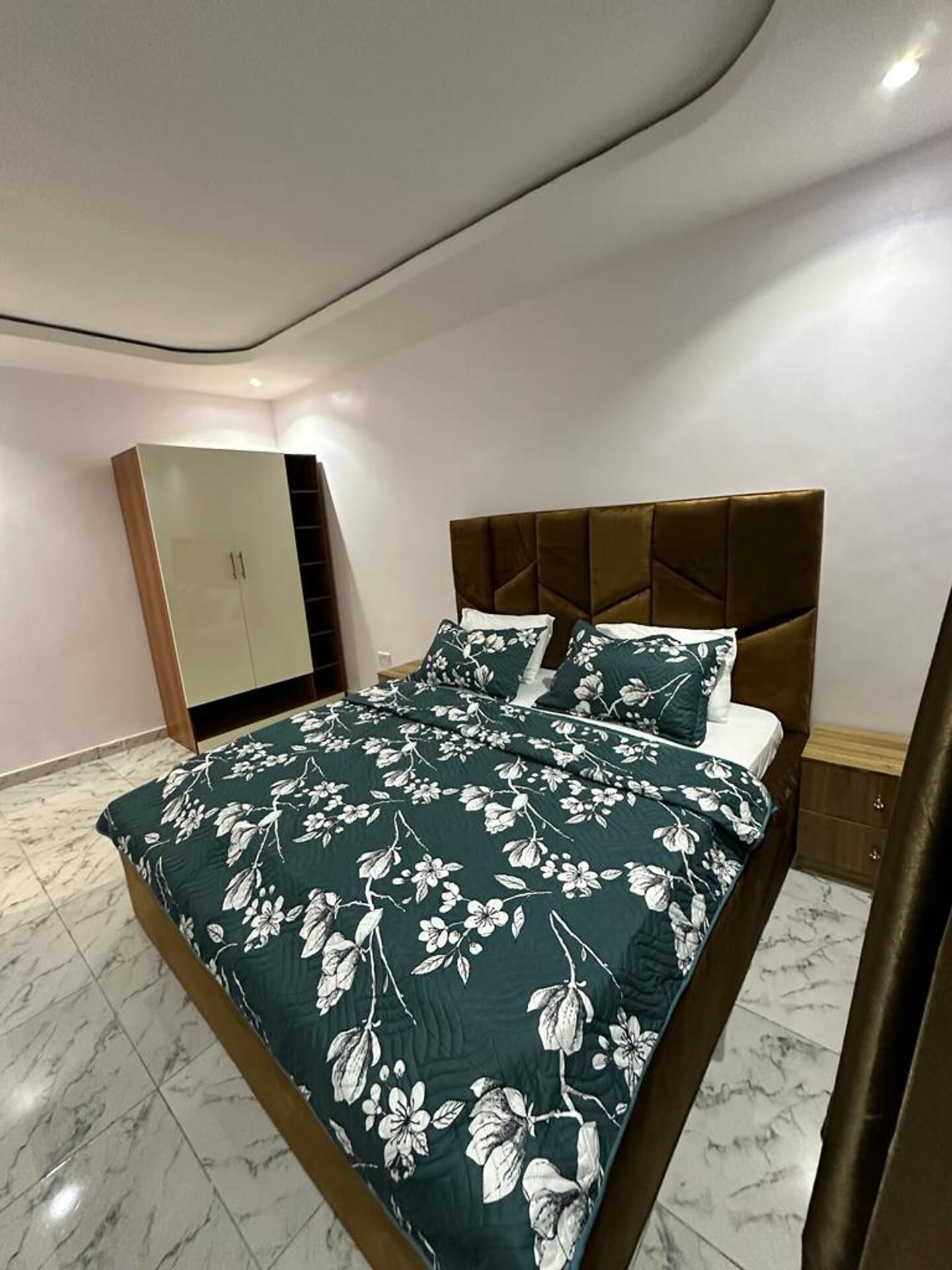 A modern bedroom with a bed, a wardrobe, and a marble floor.
