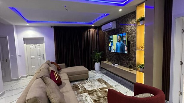 Una sala de estar moderna con un sofá seccional, un sillón rojo, un televisor de pantalla plana y un estante decorativo.
