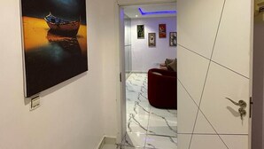 Un pasillo con un cuadro grande de un barco al atardecer, que conduce a una habitación con una silla roja y una puerta con diseño de mosaicos geométricos.