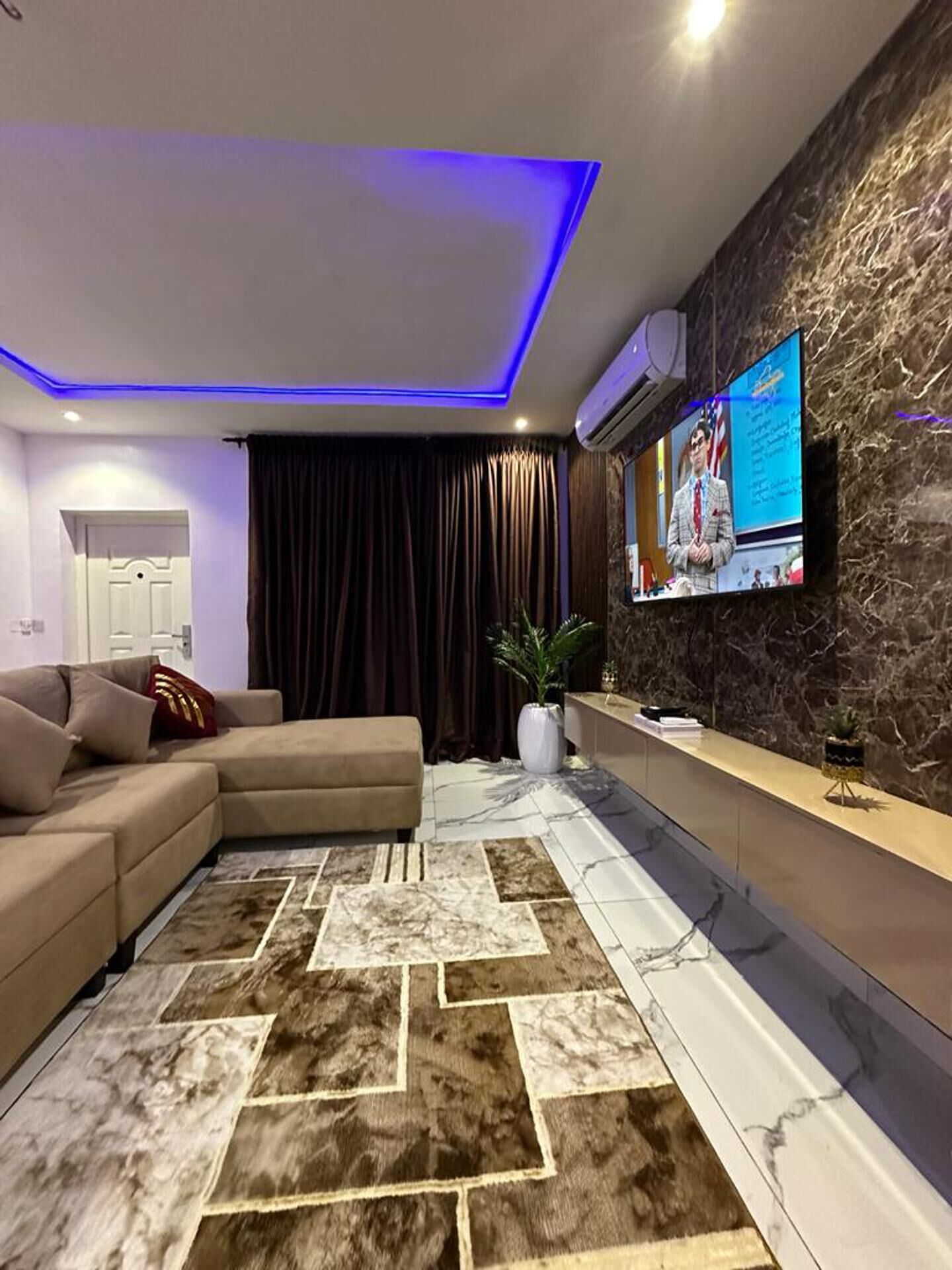 Ein modernes Wohnzimmer mit einem Ecksofa, einem Teppich mit Marmormuster und einer Wand mit Steinverkleidung.