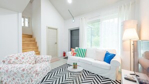 Ein modernes Wohnzimmer mit einer Couch, einem Couchtisch mit Flaschen, einem gemusterten Teppich und einer Treppe.