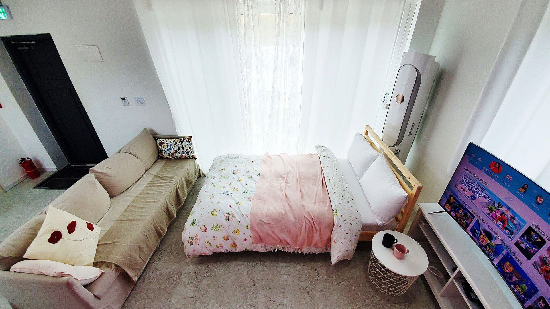 Un dormitorio con cama, sofá, televisión y una mesita.