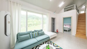 Ein modernes Wohnzimmer mit einer Couch, einem Couchtisch mit Flaschen, einer Treppe und Blick ins Grüne.