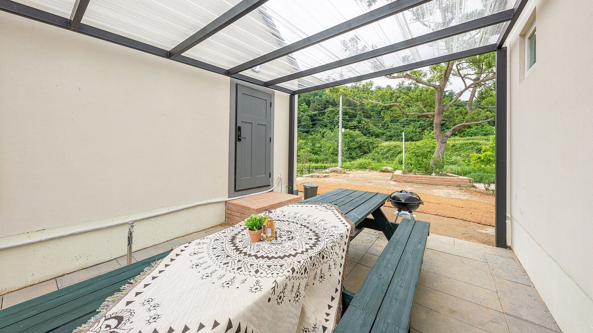 Un patio techado con una mesa para dos, una parrilla y vistas a un jardín.