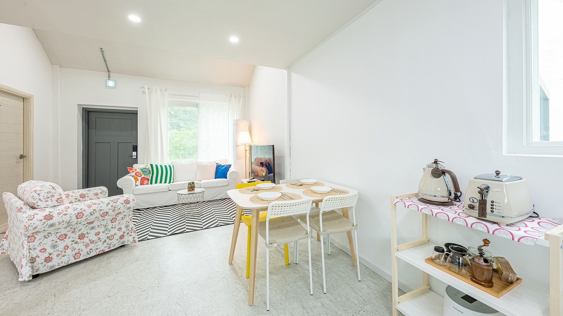 Un espacio habitable compacto con sofá, una mesa de comedor con sillas, una cafetera y una pequeña zona de cocina con tostadora.