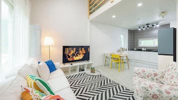 Una sala de estar moderna con un televisor de pantalla plana, un sofá, una mesa de comedor con sillas y una zona de cocina con encimera y armarios.