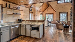 A cabin-style kitchen with wooden walls, a marble countertop, and a dining area with a stone fireplace.