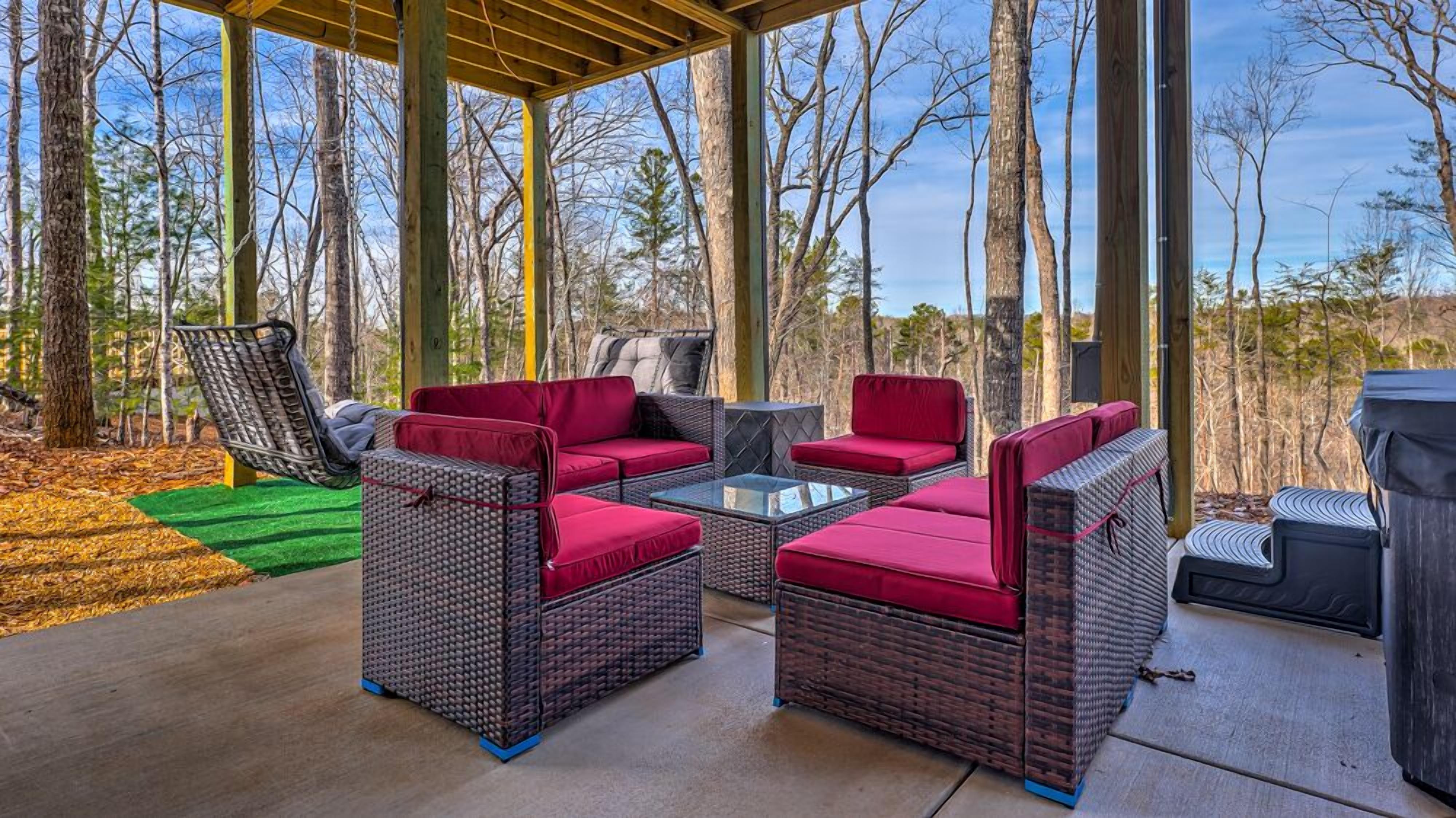 Un patio al aire libre con mobiliario de mimbre y una mesa de vidrio, rodeado de árboles.