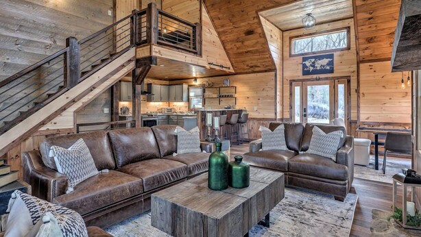 A spacious living area with a large brown leather sofa set, a wooden coffee table, and a staircase leading to an upper level.