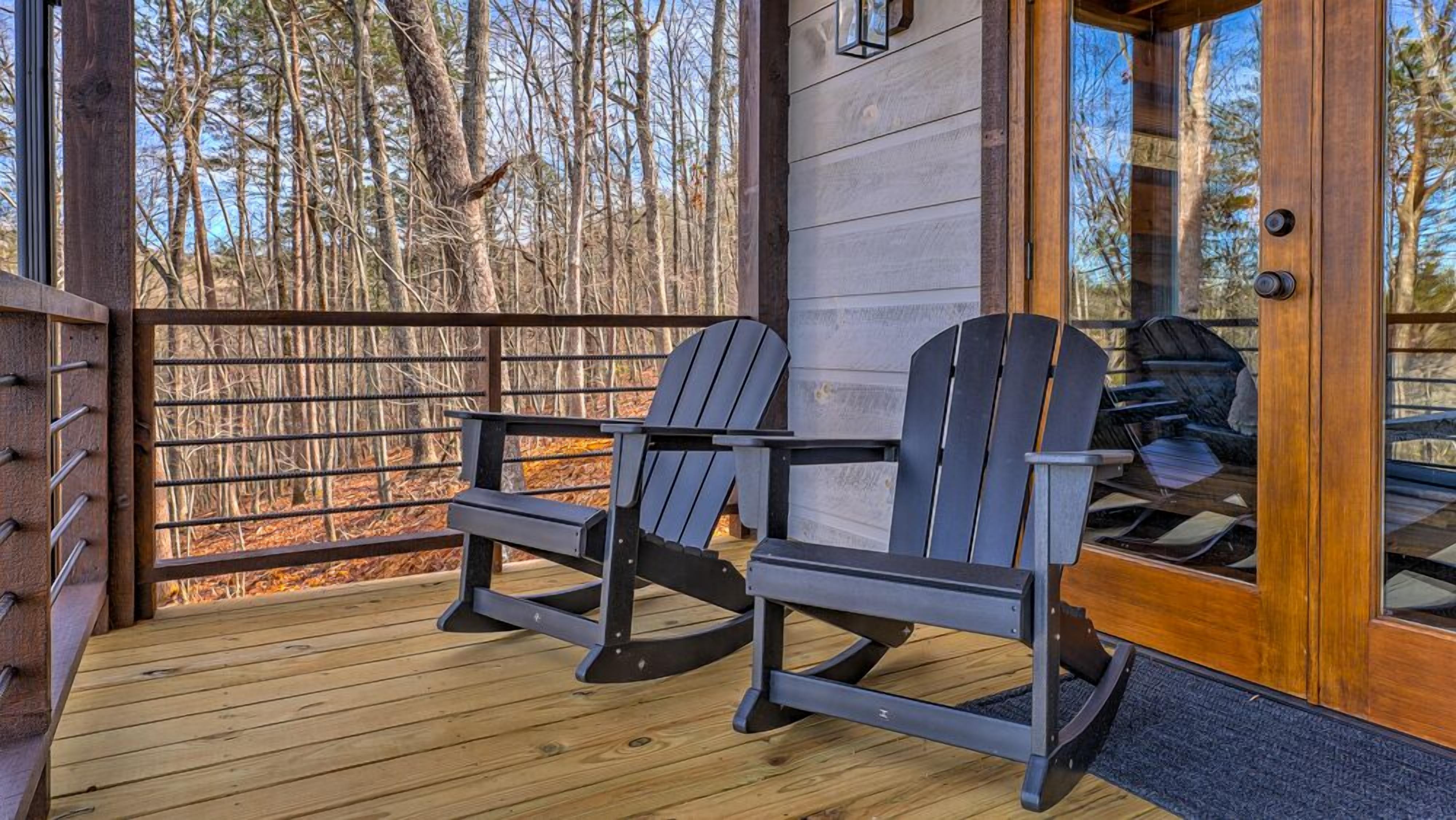 A wooden deck with two Adirondack chairs, a wooden door, and a view of a forest.