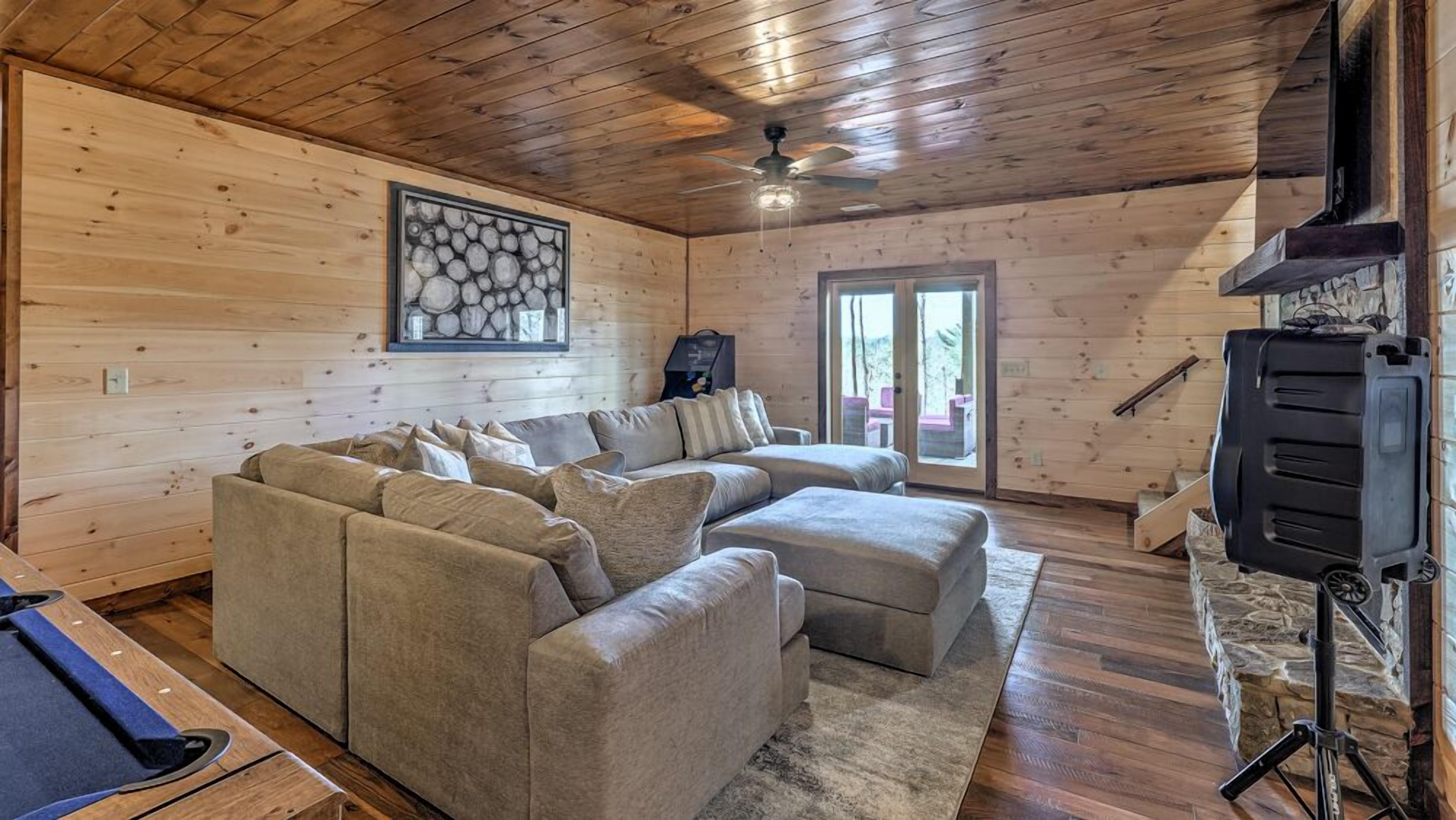 A cozy cabin interior with a sectional sofa, a ceiling fan, and a stone fireplace.