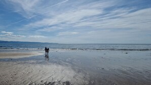 A beach with a person walking towards the water. - Memorymakersholiday Sea View (Pwllheli)
