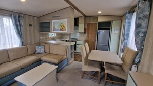 A compact living space with a sofa, a dining table, and a kitchenette. - Memorymakersholiday Sea View (Pwllheli)