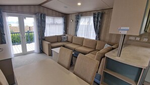 A compact living area with a sofa, a dining table, and curtains. - Memorymakersholiday Sea View (Pwllheli)