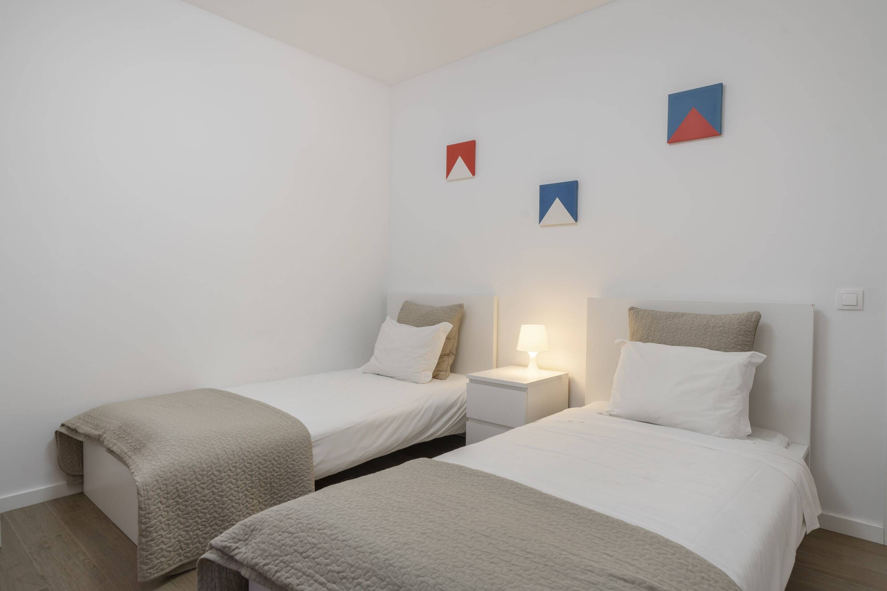 Een slaapkamer met twee eenpersoonsbedden, een nachtkastje met een lamp, en geometrische decoratie aan de muur.