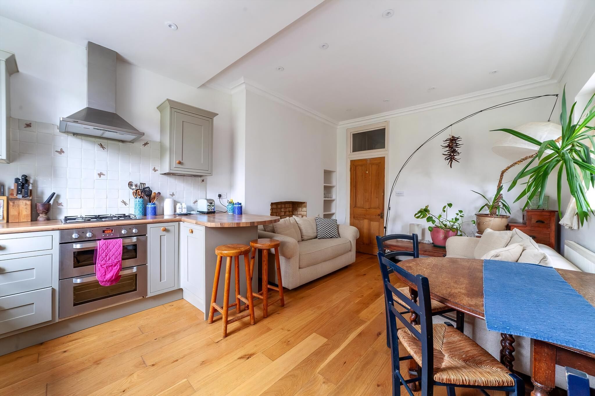 A compact kitchen with a central island, wooden stools, a dining table with chairs, and a sofa in a living area.