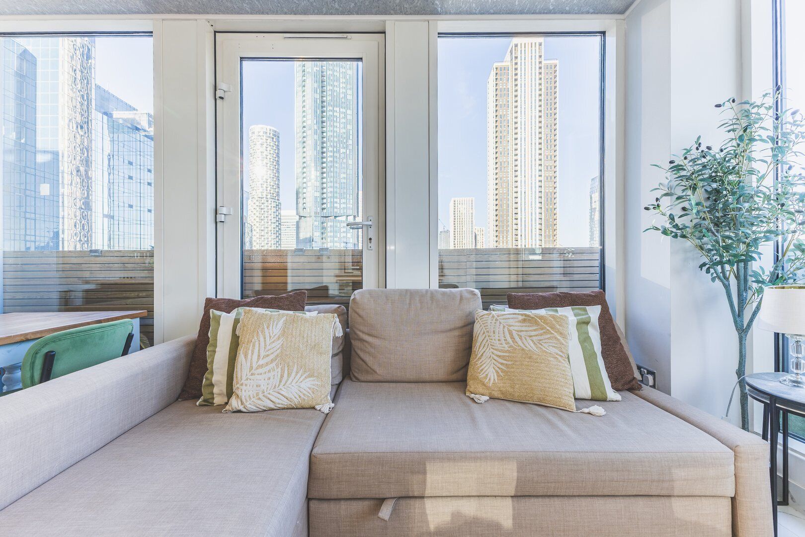 A modern living room with a beige sofa, two side tables, and a potted plant.