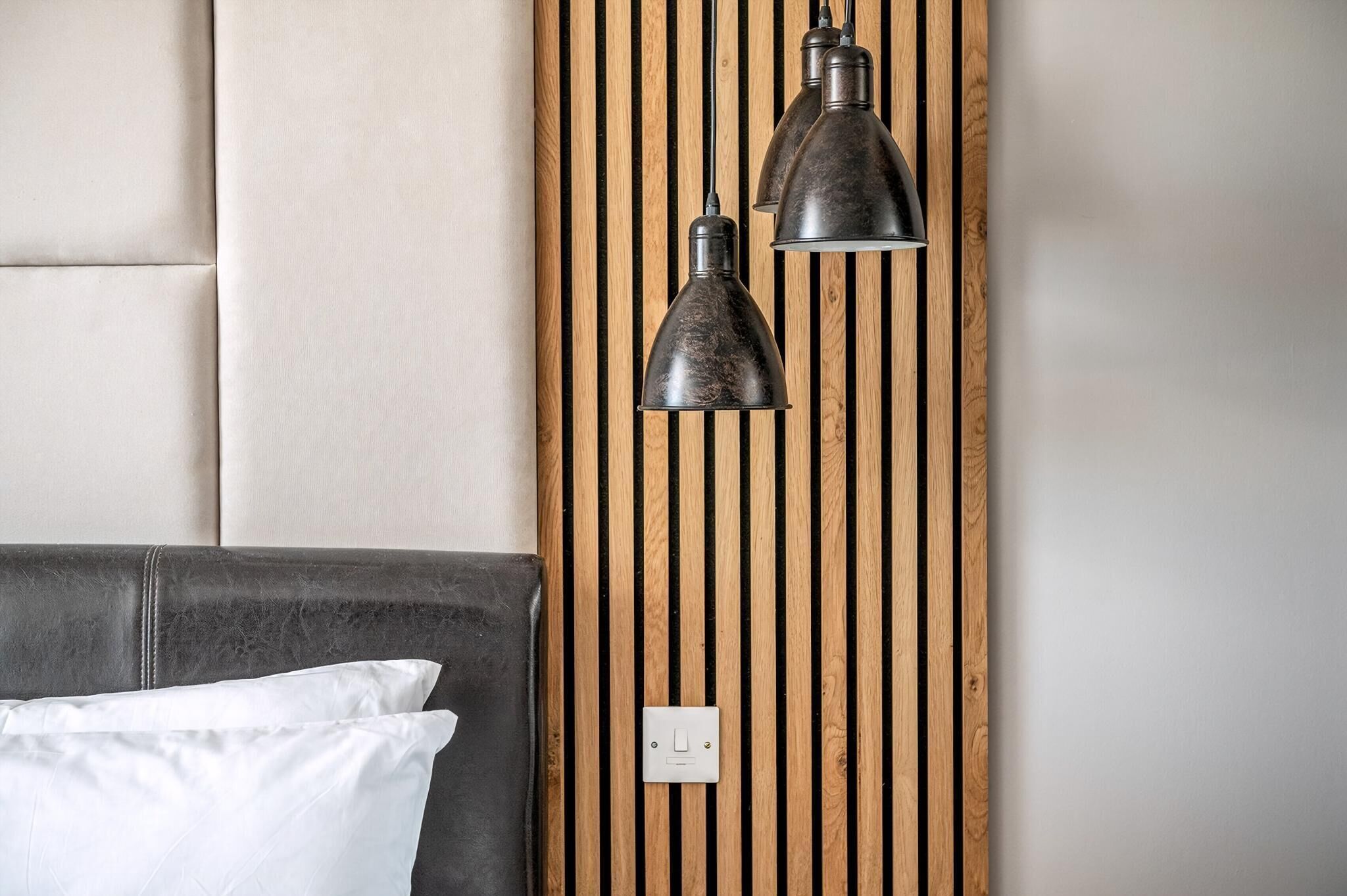 A bed with a headboard, a wooden slat wall panel, and two pendant lights.