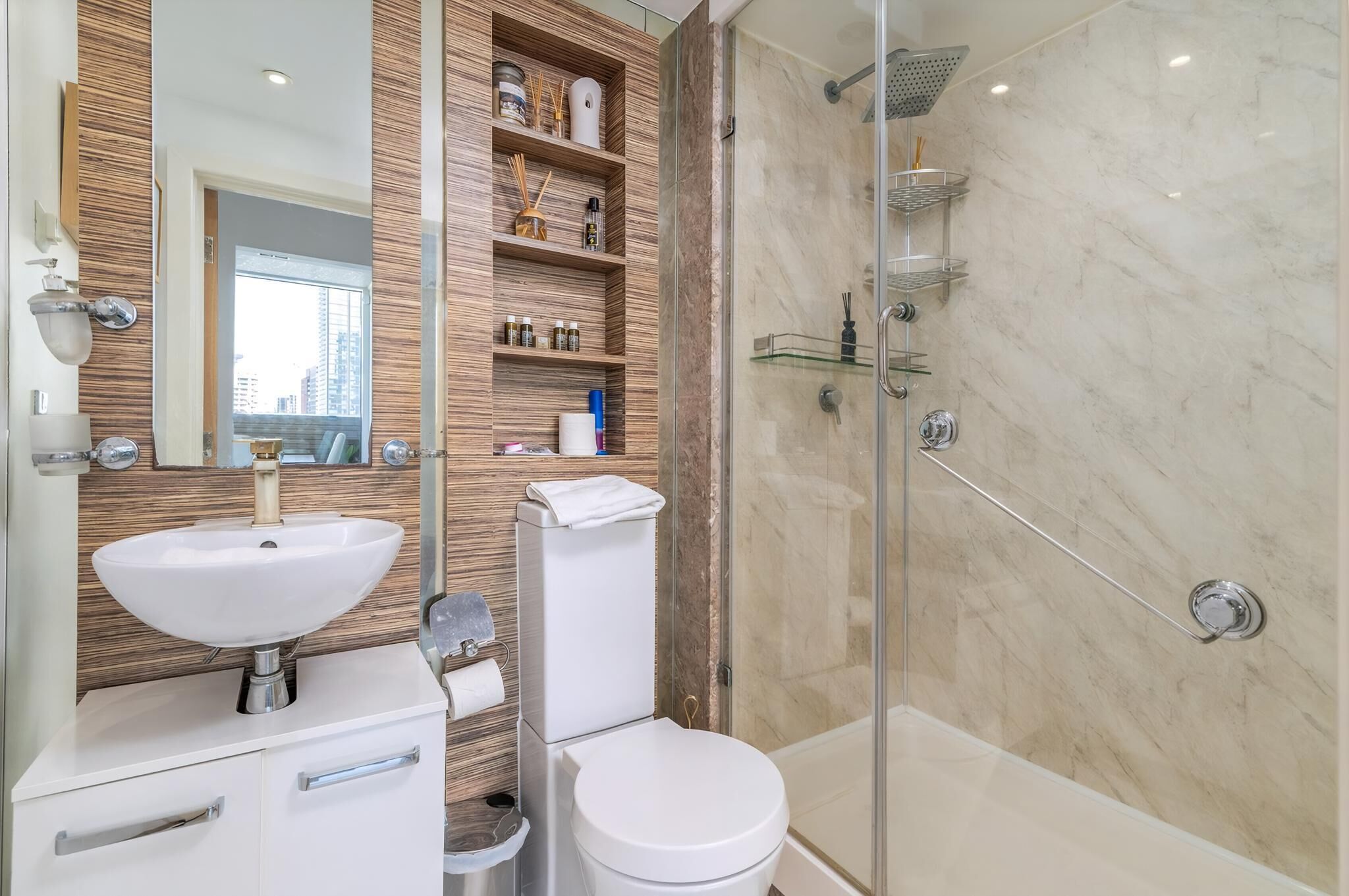 A modern bathroom with a large mirror, a white sink, a toilet, and a glass-enclosed shower area.