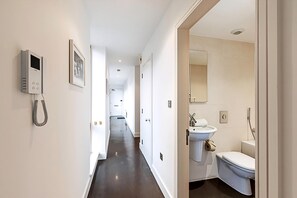 A hotel hallway with a phone, framed picture, and a view into a bathroom with a sink and toilet. - Comfortable, Modern Flat in Shoreditch (London)