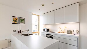 A modern kitchen with white cabinetry, a large island, and a view of the city. - Comfortable, Modern Flat in Shoreditch (London)
