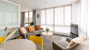 A modern living room with a sofa, chairs, a TV, and a large window with curtains. - Comfortable, Modern Flat in Shoreditch (London)