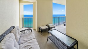 A balcony with wicker furniture, a glass table, and a view of the ocean.