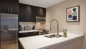 A modern kitchen with dark cabinets, stainless steel appliances, a white countertop, and a sink with a unique faucet.
