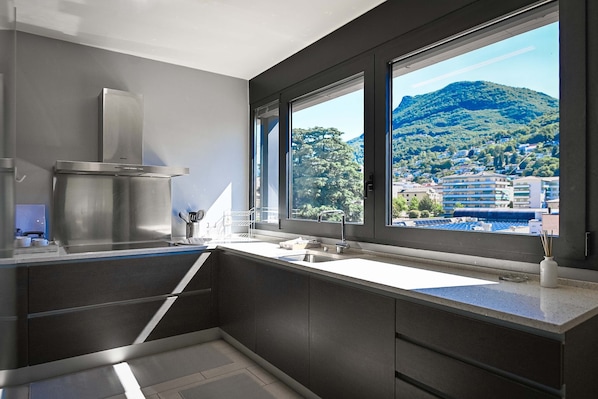 A modern kitchen with a large window, stainless steel appliances, and a view of a mountain.