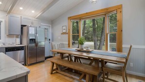 A kitchen with a stainless steel refrigerator, wooden bench seating, and a large window with a view of trees. - Torch Lake cabin, 4BR, Sleeps 10, Firepit, A/C (Rapid City)