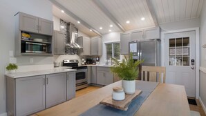 A modern kitchen with grey cabinets, a built-in microwave, stainless steel appliances, and a wooden dining table with a plant centerpiece. - Torch Lake cabin, 4BR, Sleeps 10, Firepit, A/C (Rapid City)