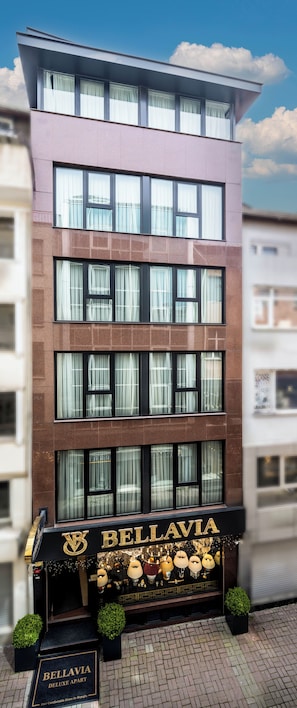Ein mehrstöckiges Gebäude mit einer Schaufensterfront, auf der 'BELLAVIA DELUXE APART' steht, mit verschiedenen dekorativen Elementen.