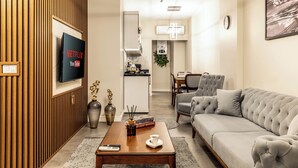 A modern living room with a flat-screen TV, a coffee table with books and a remote, a sofa, and a dining area in the background. - Bellavia Deluxe Apart (Istanbul)