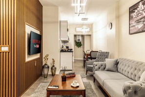 Ein modernes Wohnzimmer mit Flachbildfernseher, Couchtisch mit Büchern und Fernbedienung, Sofa und Essbereich im Hintergrund.